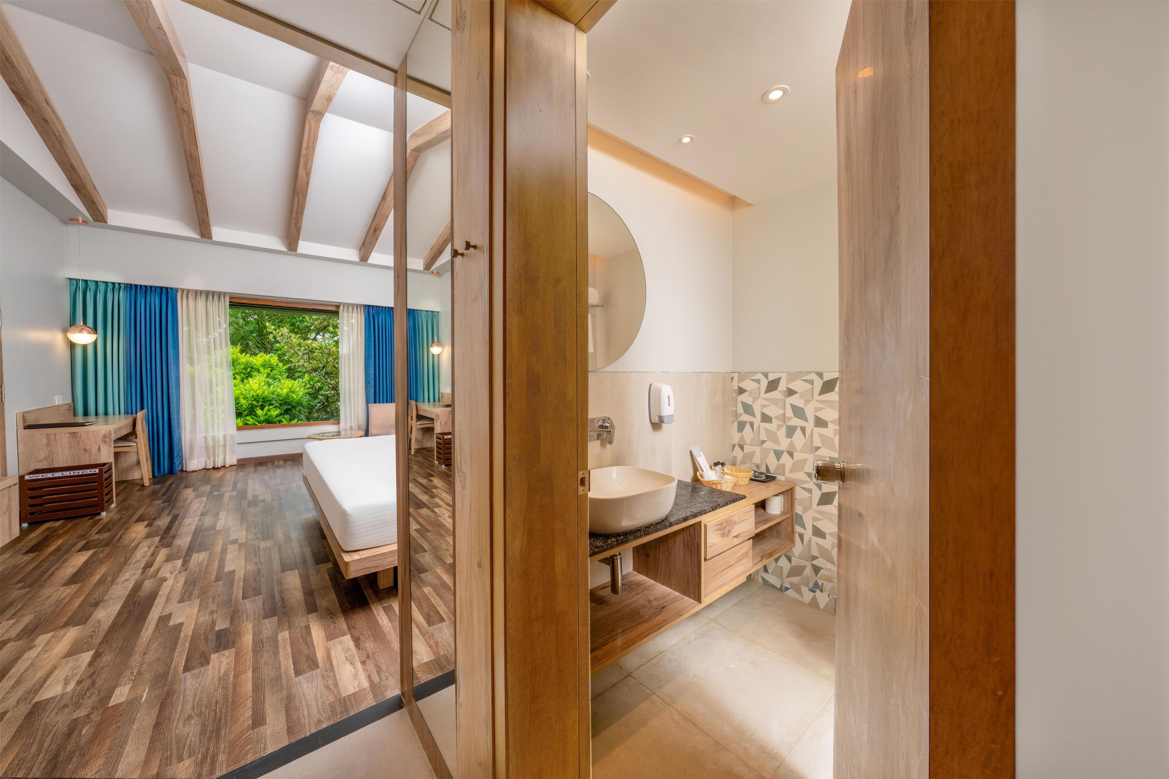 Un dormitorio moderno con techo de madera, una cama grande, un escritorio y vistas a zonas verdes.