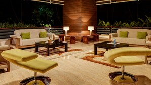 A modern living room with a central wooden pillar, two sofas with green cushions, a coffee table, and a yellow accent chair. - Purple Palms Resort & Spa (Somvarpet)