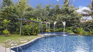 A swimming pool with a mosaic tile design, surrounded by lush greenery and palm trees. - Purple Palms Resort & Spa (Somvarpet)