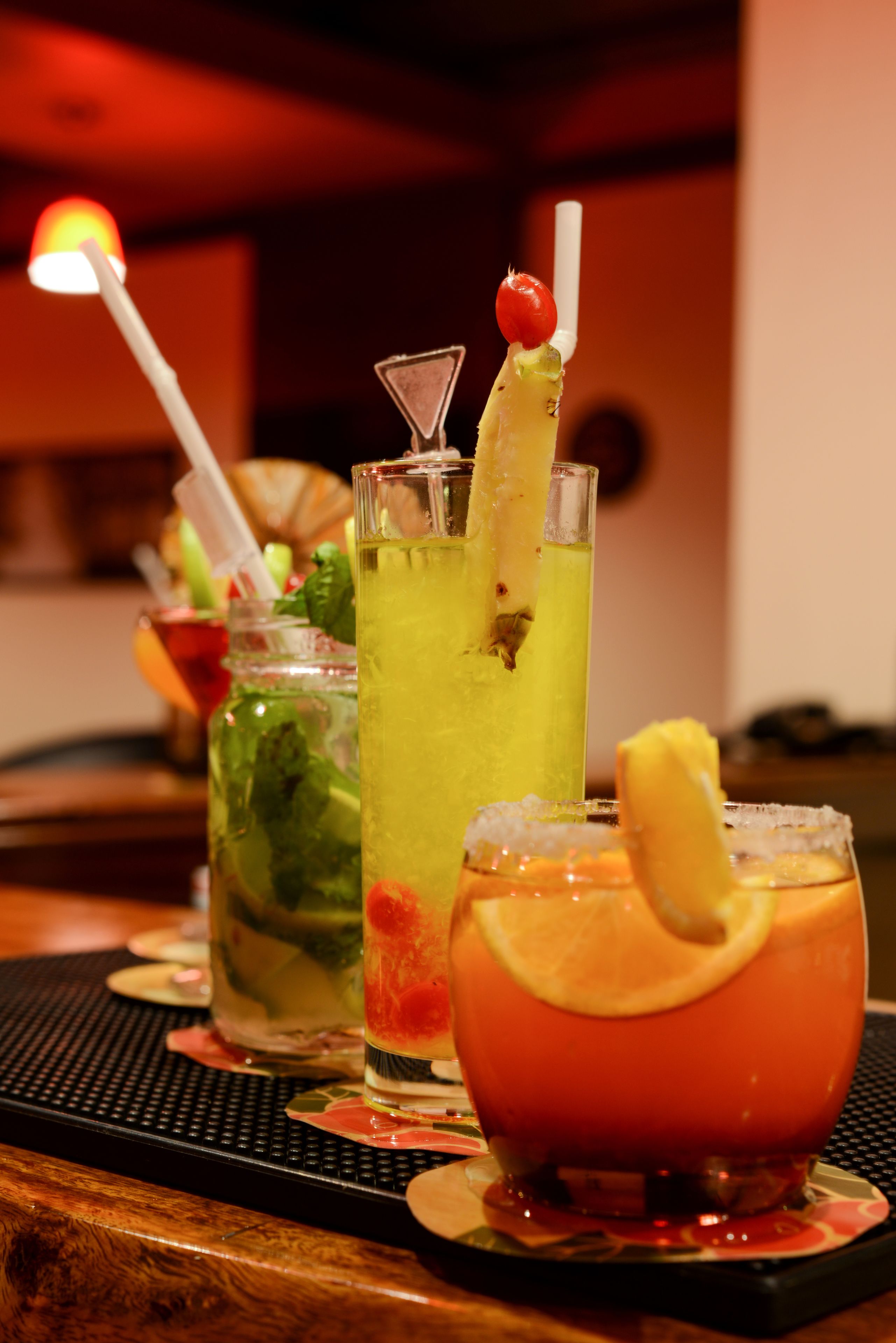 A bar with three different cocktails, each with unique garnishes and straws.