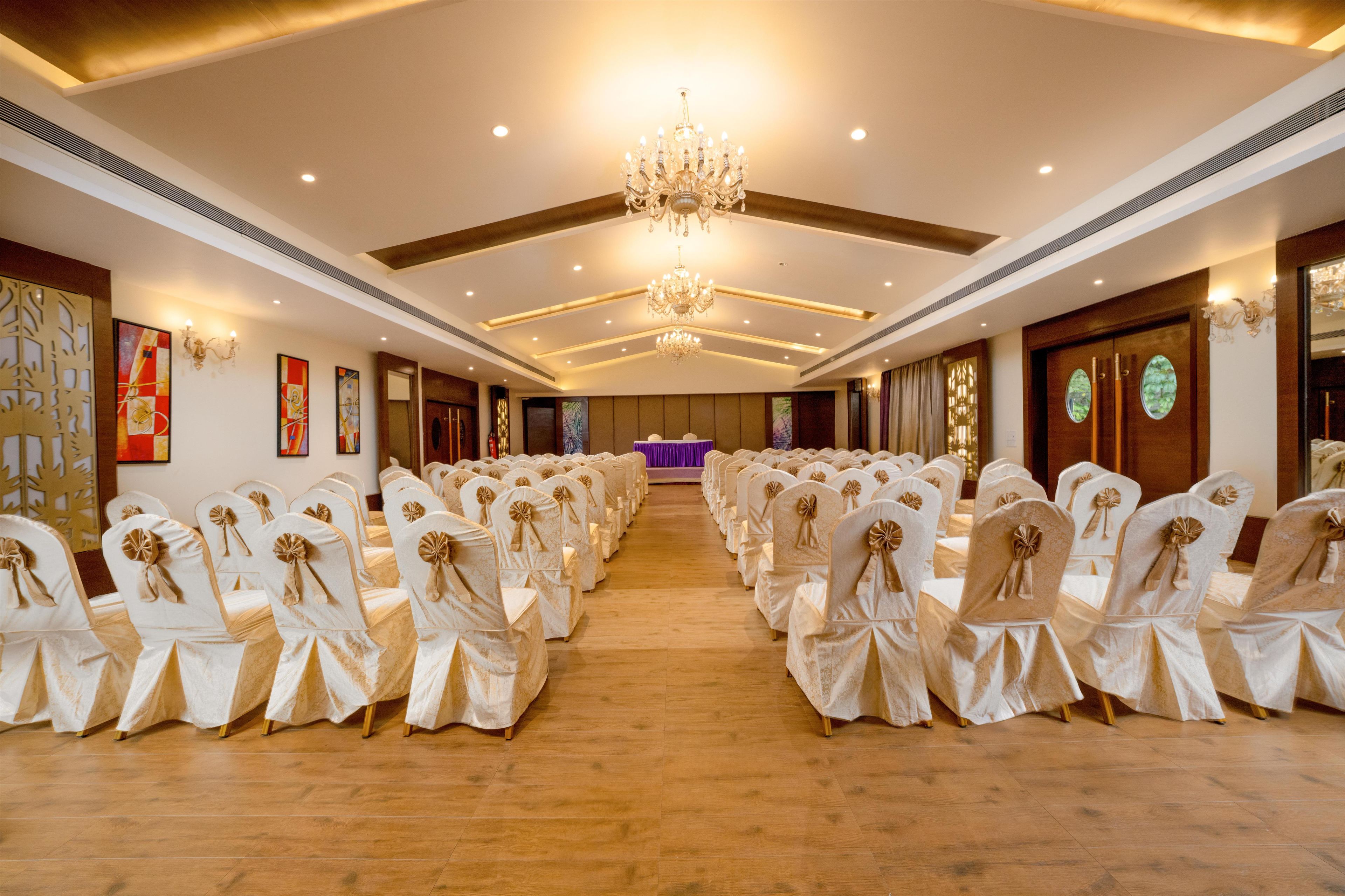 A hotel conference room with rows of chairs, a chandelier, and wall art.