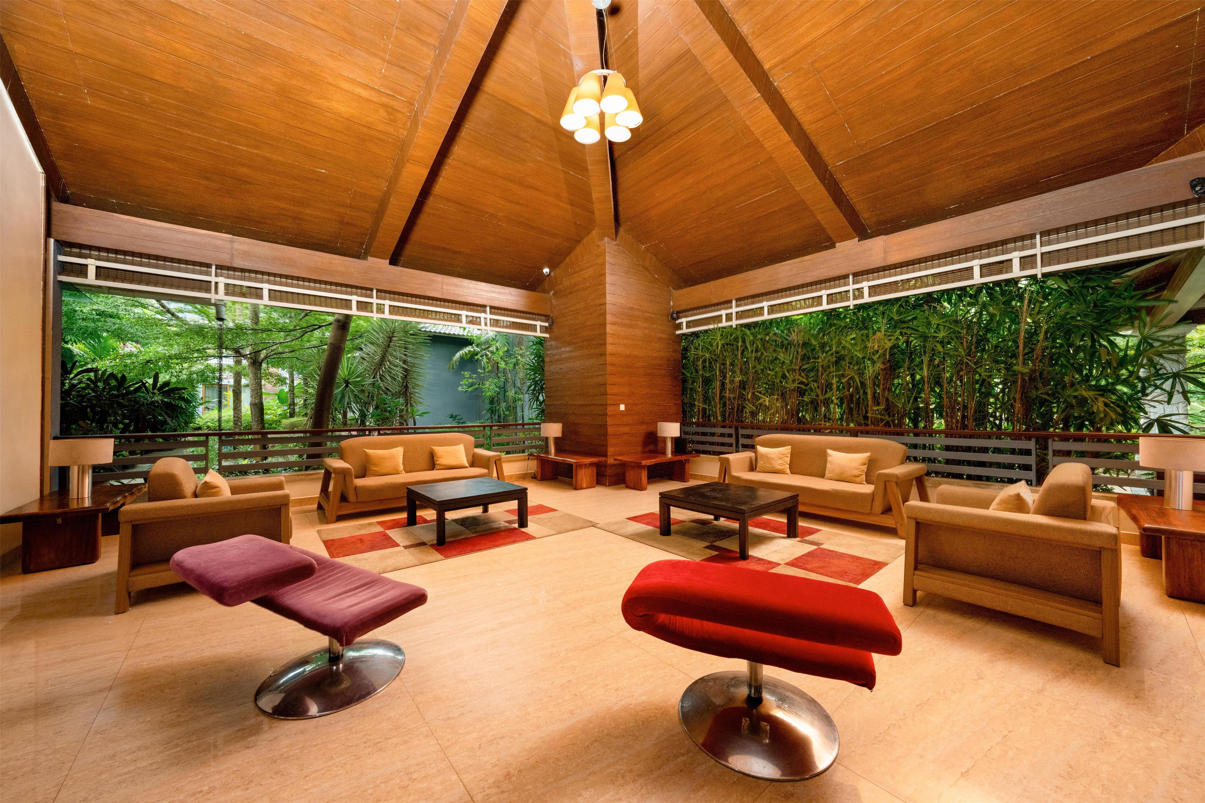 A spacious indoor area with wooden ceiling and large windows, featuring sofas, a coffee table, and a red ottoman.