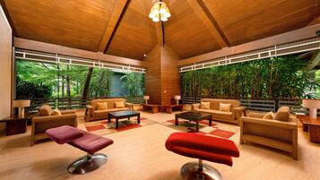 A spacious indoor area with wooden ceiling and large windows, featuring sofas, a coffee table, and a red ottoman.