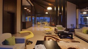 A modern hotel lobby with a reception desk, seating areas, and a view of the cityscape. - Purple Palms Resort & Spa (Somvarpet)