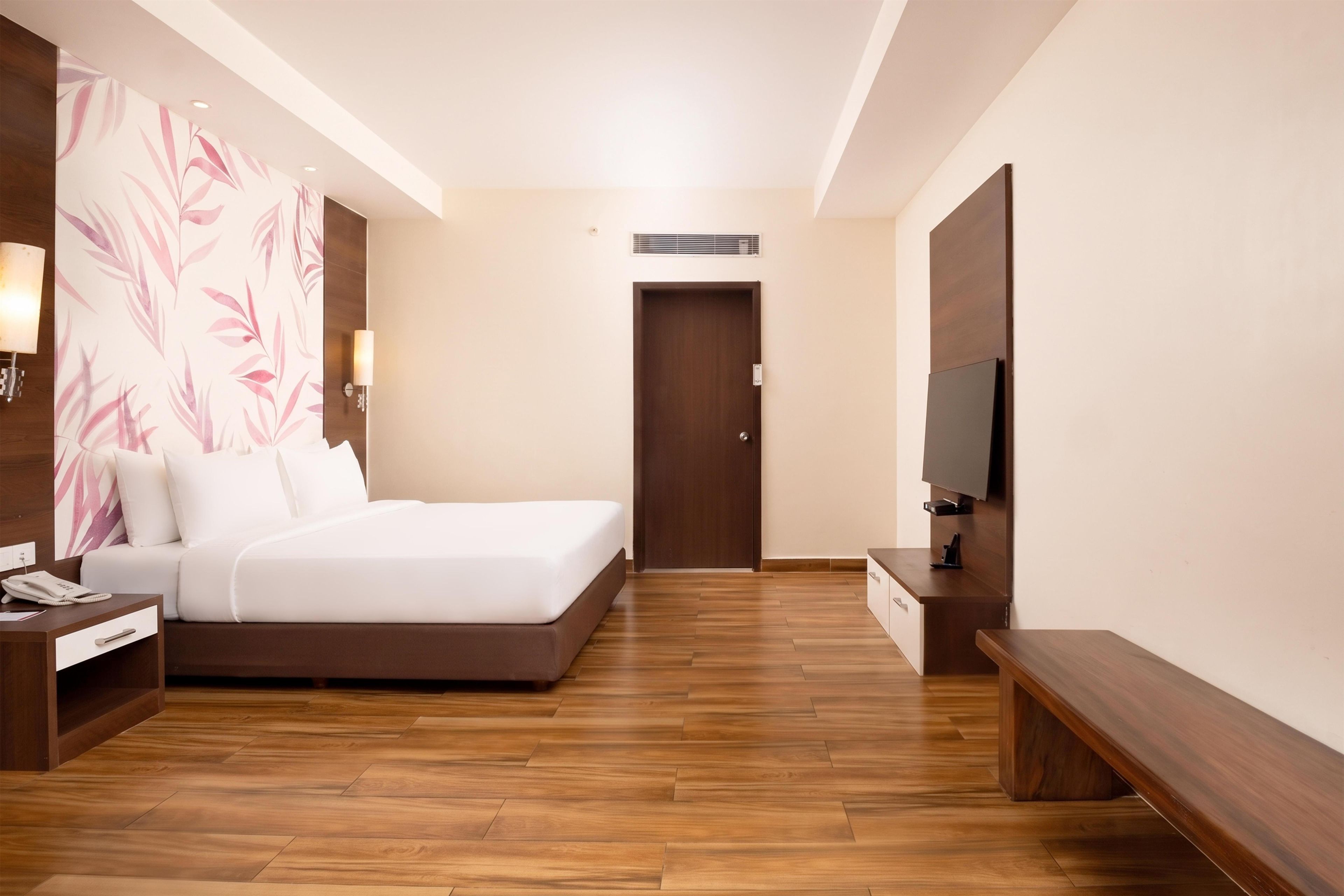 A hotel room with a bed, bedside table, lamp, and a television on a stand.