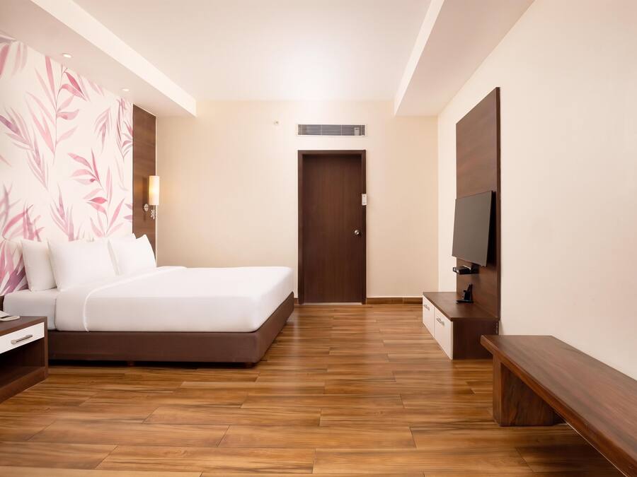 A hotel room with a bed, bedside table, lamp, and a television on a stand.