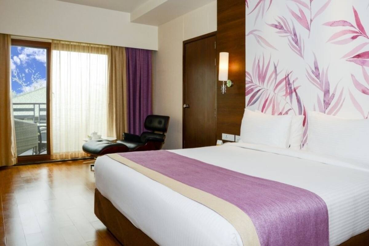 Quarto de hotel com uma cama grande, uma cadeira, uma escrivaninha e vista para o exterior.