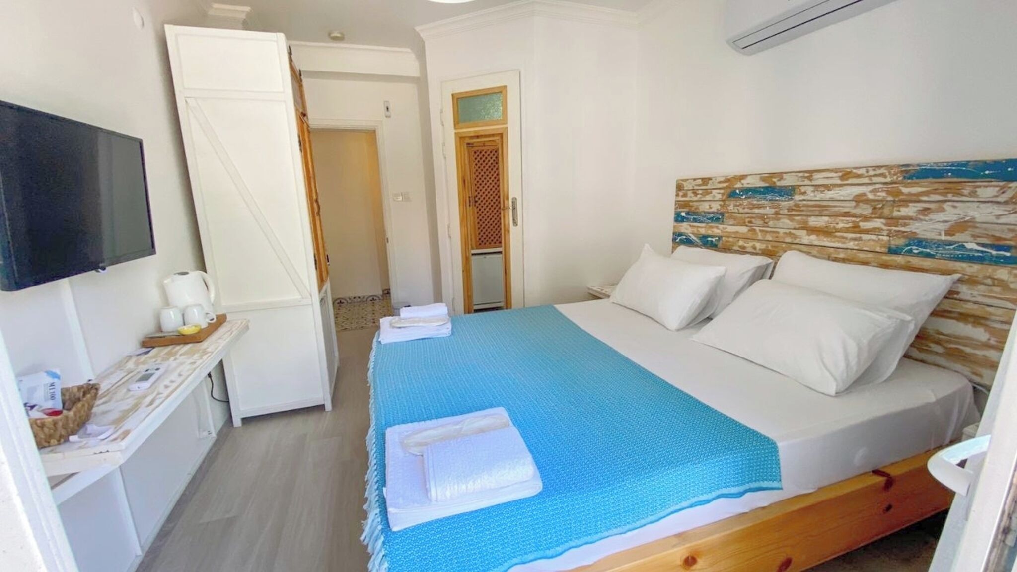 Ein Hotelzimmer mit Bett, Fernseher, Schreibtisch mit Computer und einem durchgegangenen Tür erkennbaren Badezimmer.