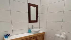 A bathroom with a wooden vanity, a white sink, a mirror, a toilet, and patterned floor tiles. - Merih Hotel (Bodrum)