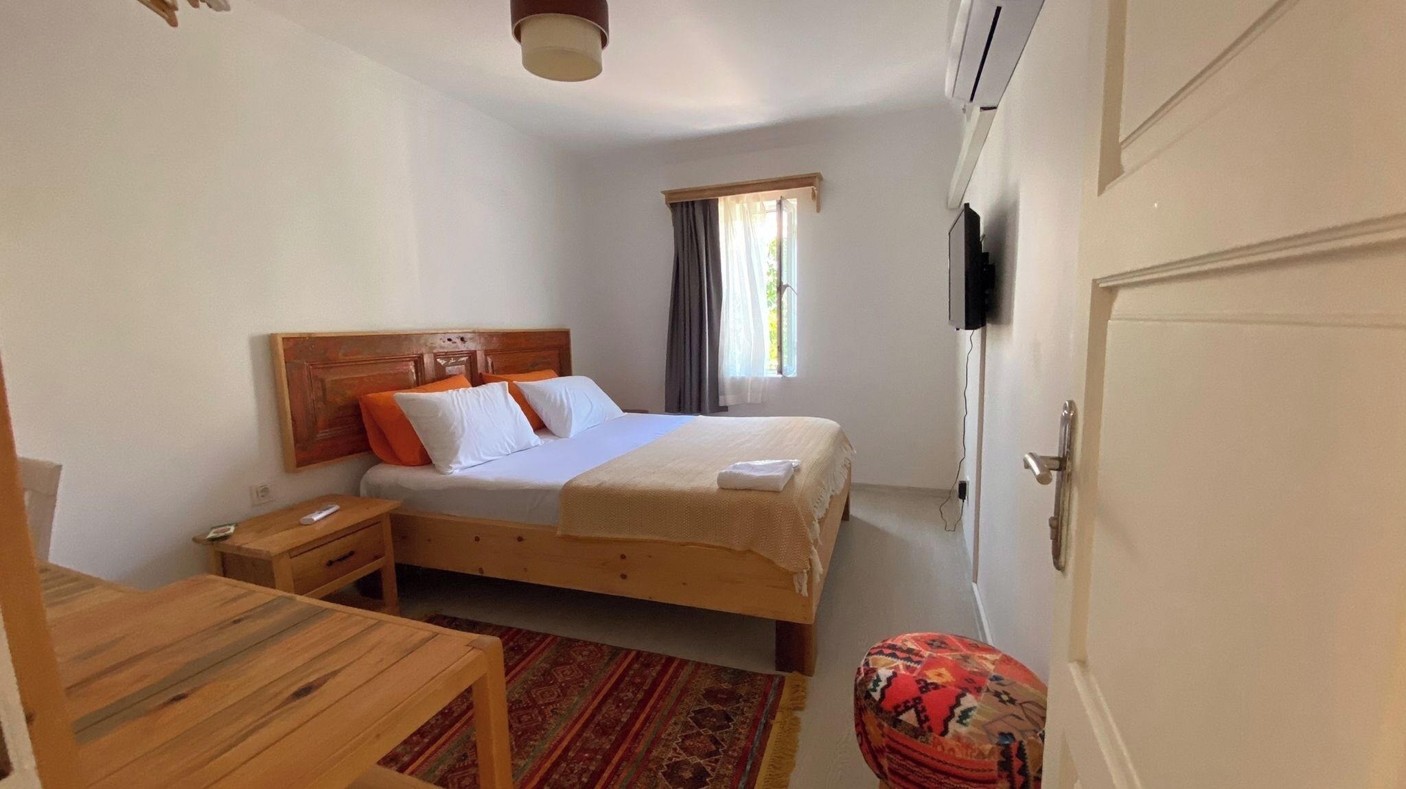Ein Schlafzimmer mit Bett, Nachttisch, Stuhl, Fernseher und einem Fenster mit Vorhängen.