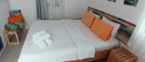 A neatly made bed with white and orange bedding, a wooden headboard, and a small wooden stool with colorful cushions.