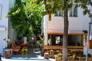 A cozy outdoor seating area with wooden tables and chairs, surrounded by potted plants and a large tree providing shade. - Merih Hotel (Bodrum)