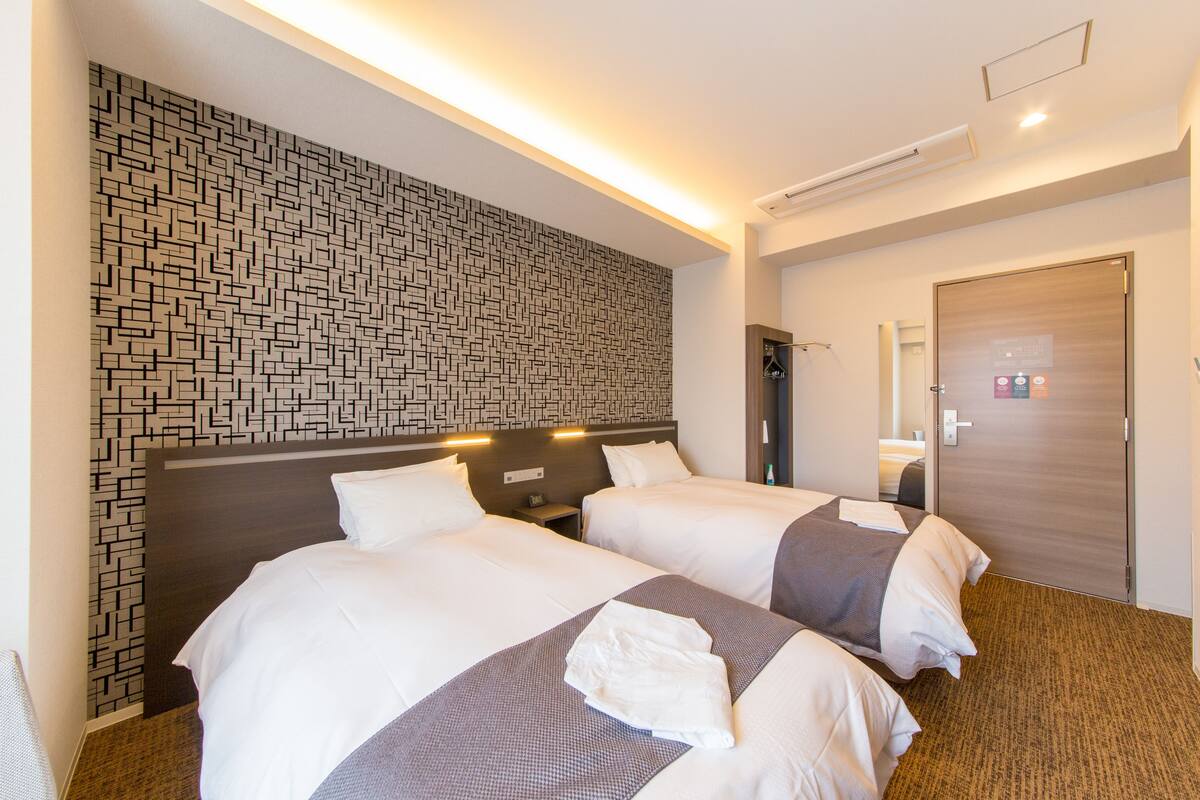 A hotel room with two beds, a patterned wall, and a wooden door.