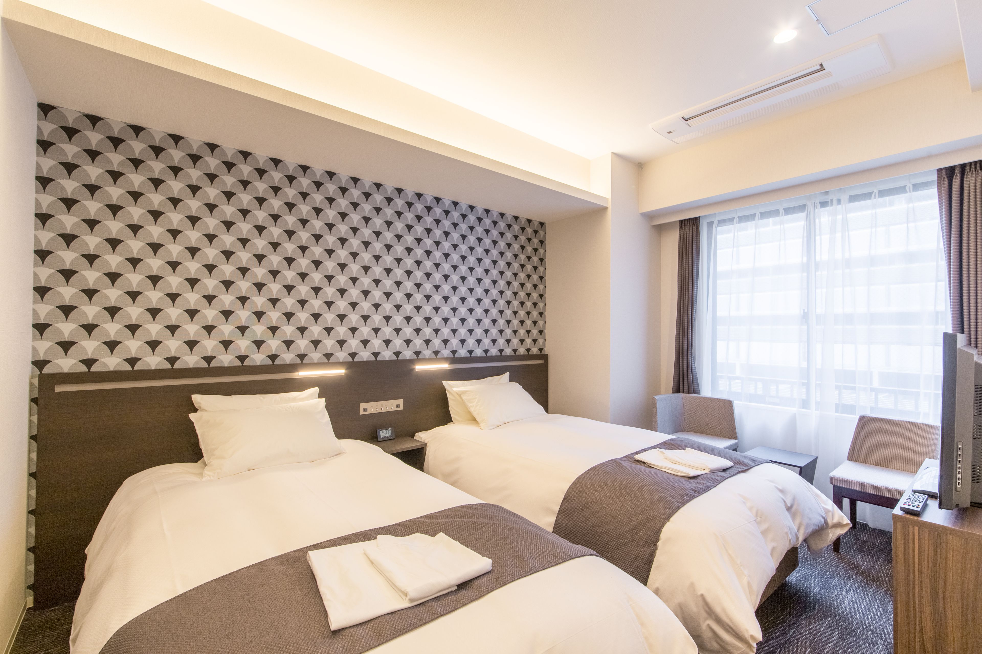A hotel room with two beds, a TV, a desk, and a window with curtains.
