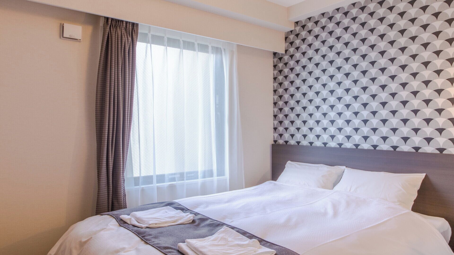 Una habitación de hotel con cama, cortinas, una ventana y un papel tapiz estampado.