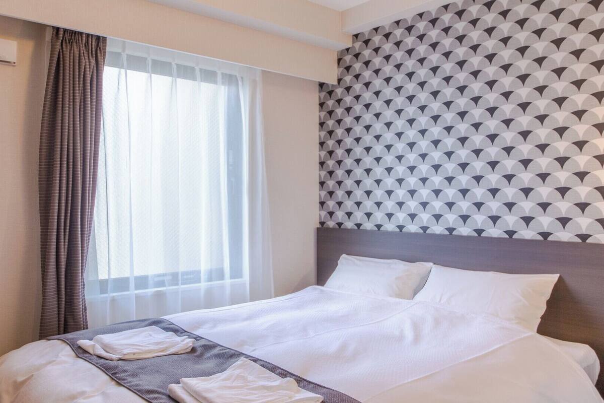 A hotel room with a bed, curtains, a window, and a patterned wall.