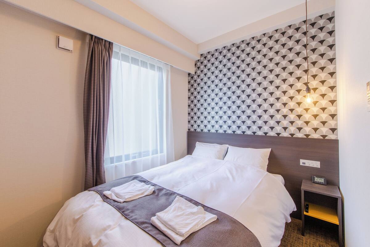 A hotel room with a bed, a nightstand, a wall clock, and a geometric patterned wall.