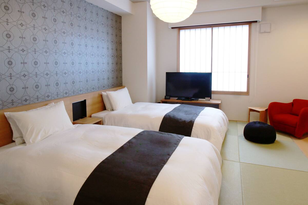 A hotel room with two beds, a TV, a red chair, and a tatami mat.