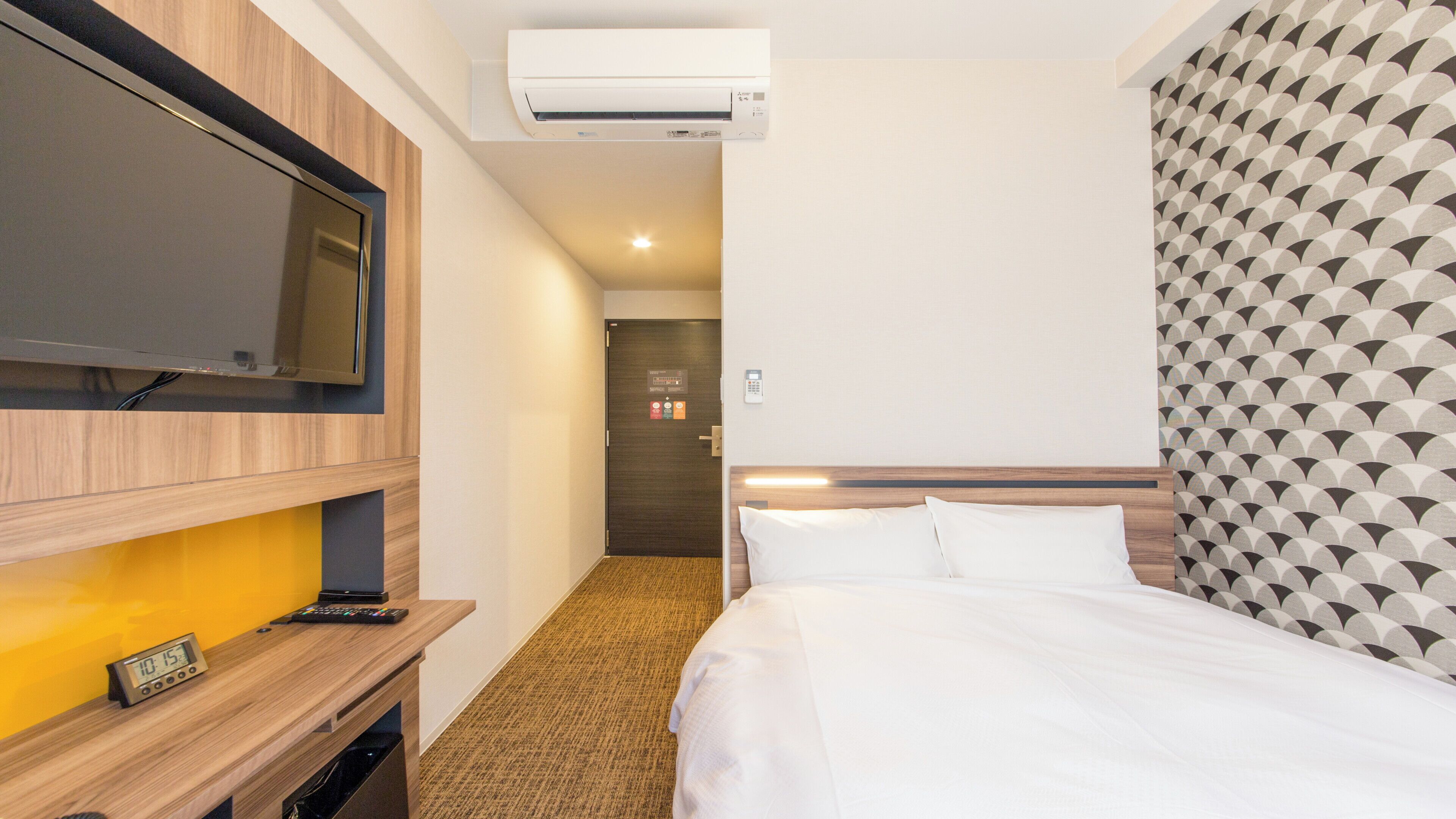 Habitación de hotel con una cama, un televisor montado en la pared, un escritorio con un control remoto y un equipo de aire acondicionado.