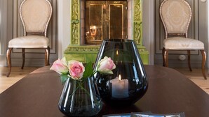 A room with a green ornate fireplace, two chairs, a table with a vase of flowers, and a candle. - Kongsvinger Castle Hotel & Resort (Kongsvinger)