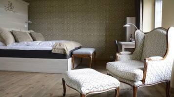 A bedroom with a bed, a chair, an ottoman, and a desk with a lamp.