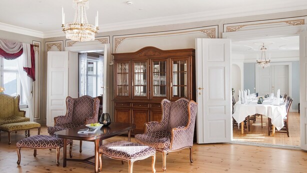 A spacious room with a wooden dining table set for a meal, surrounded by ornate chairs and a large wooden cabinet with glass doors. - Kongsvinger Castle Hotel & Resort (Kongsvinger)