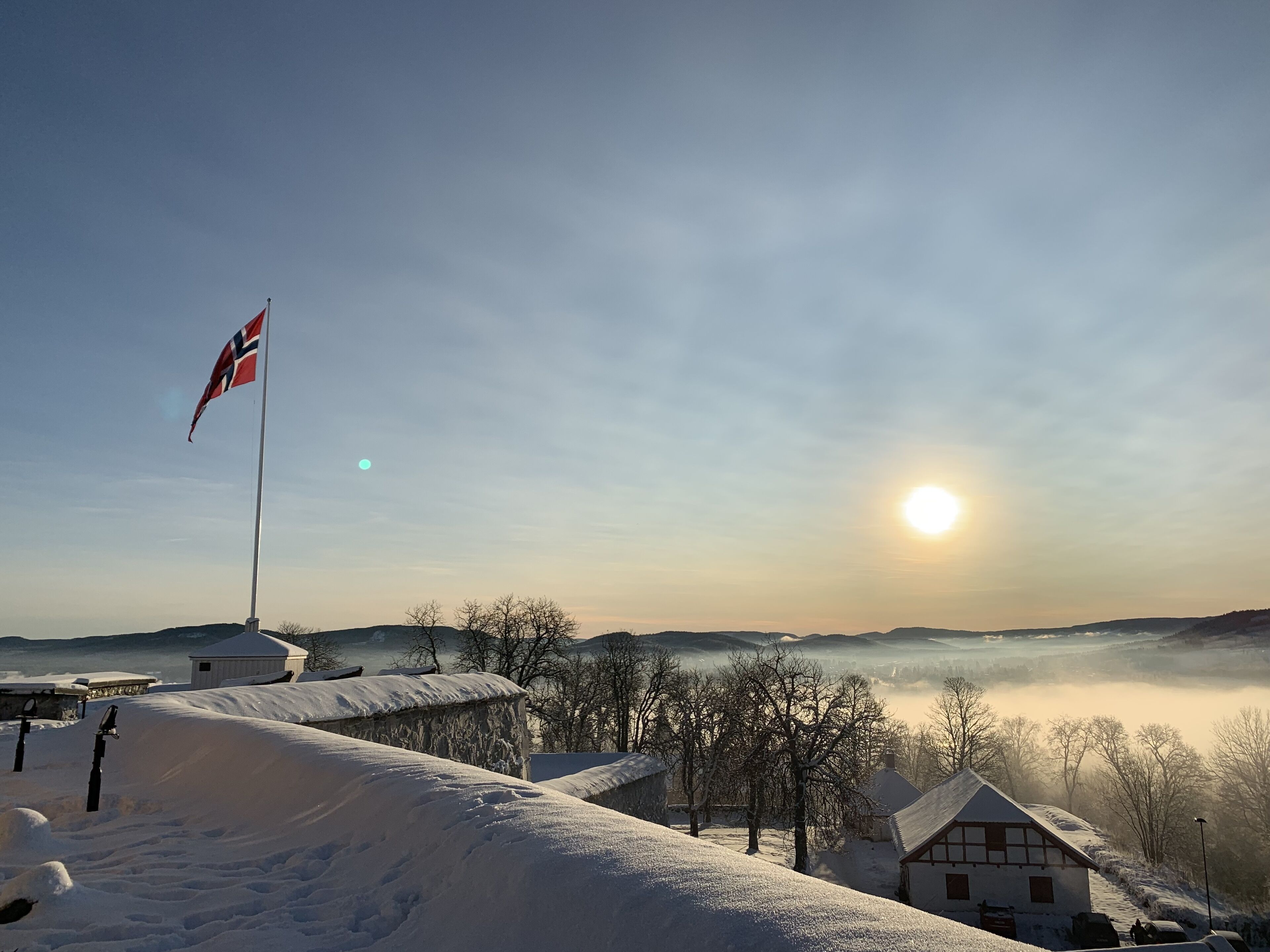 A snow-covered landscape with a flag, buildings, and a sunrise.