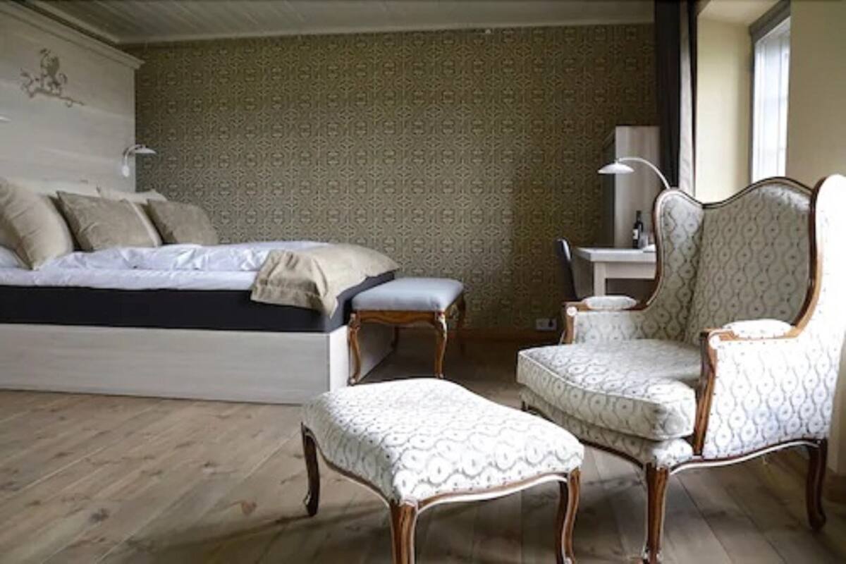 Une chambre à coucher comprenant un lit, une chaise, un pouf et un bureau avec une lampe.
