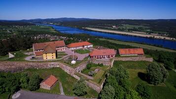 Vue aérienne d’un ensemble de bâtiments historiques comprenant plusieurs structures, une cour centrale et une rivière en arrière-plan.