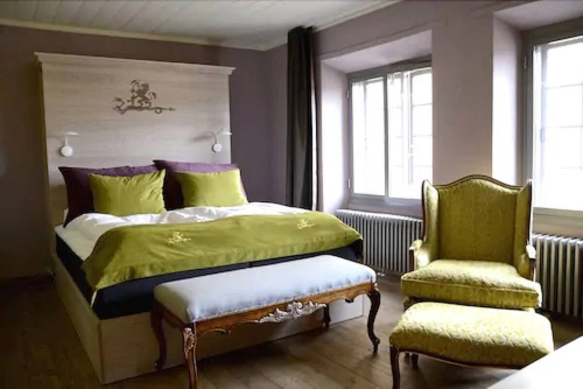 Une chambre avec un grand lit, un banc en bois et un fauteuil vert.