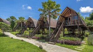Filas de bungalows de madera con techos de paja, rodeados de exuberante vegetación y palmeras.