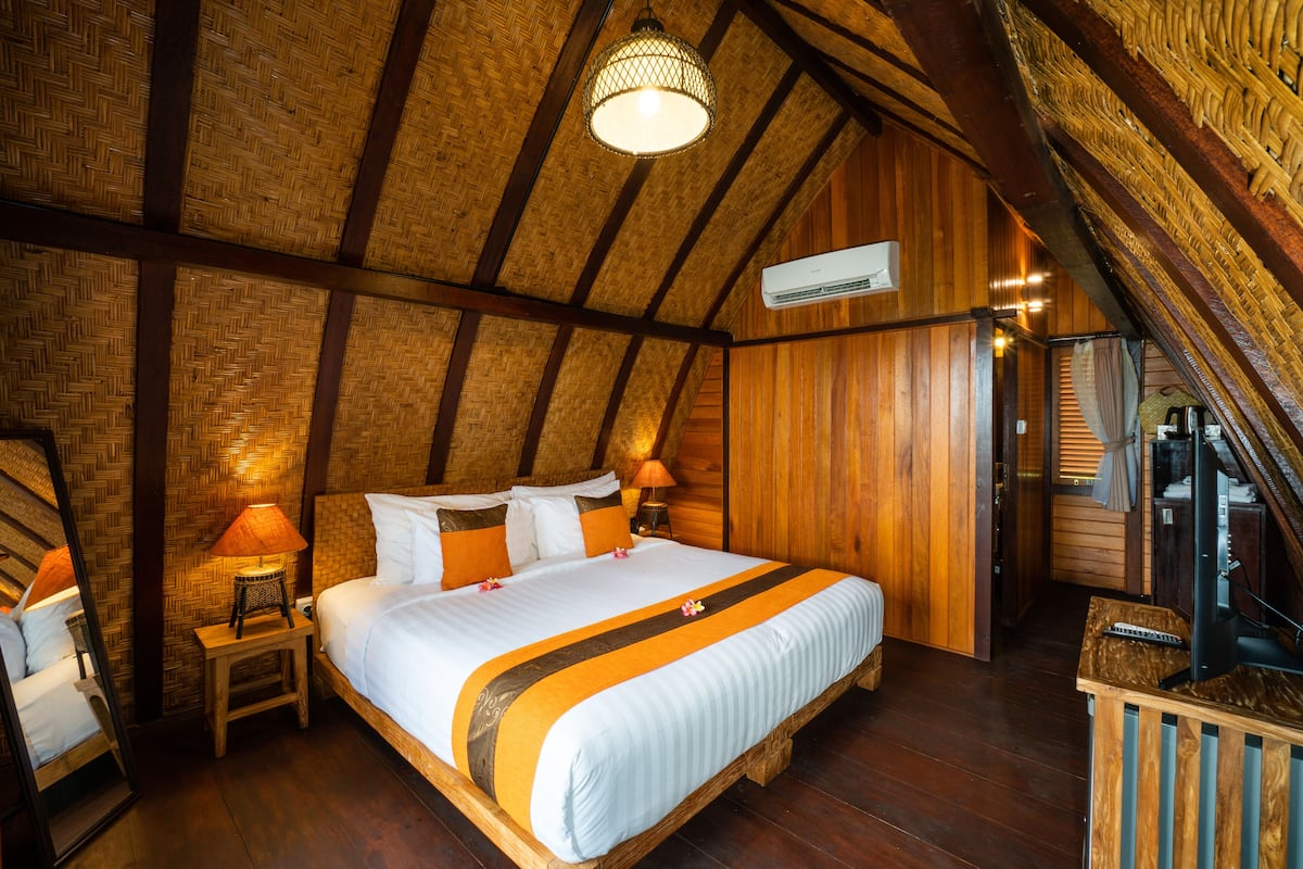 A cozy, wooden-floored bedroom with a large bed, a nightstand, a lamp, and a mirror.
