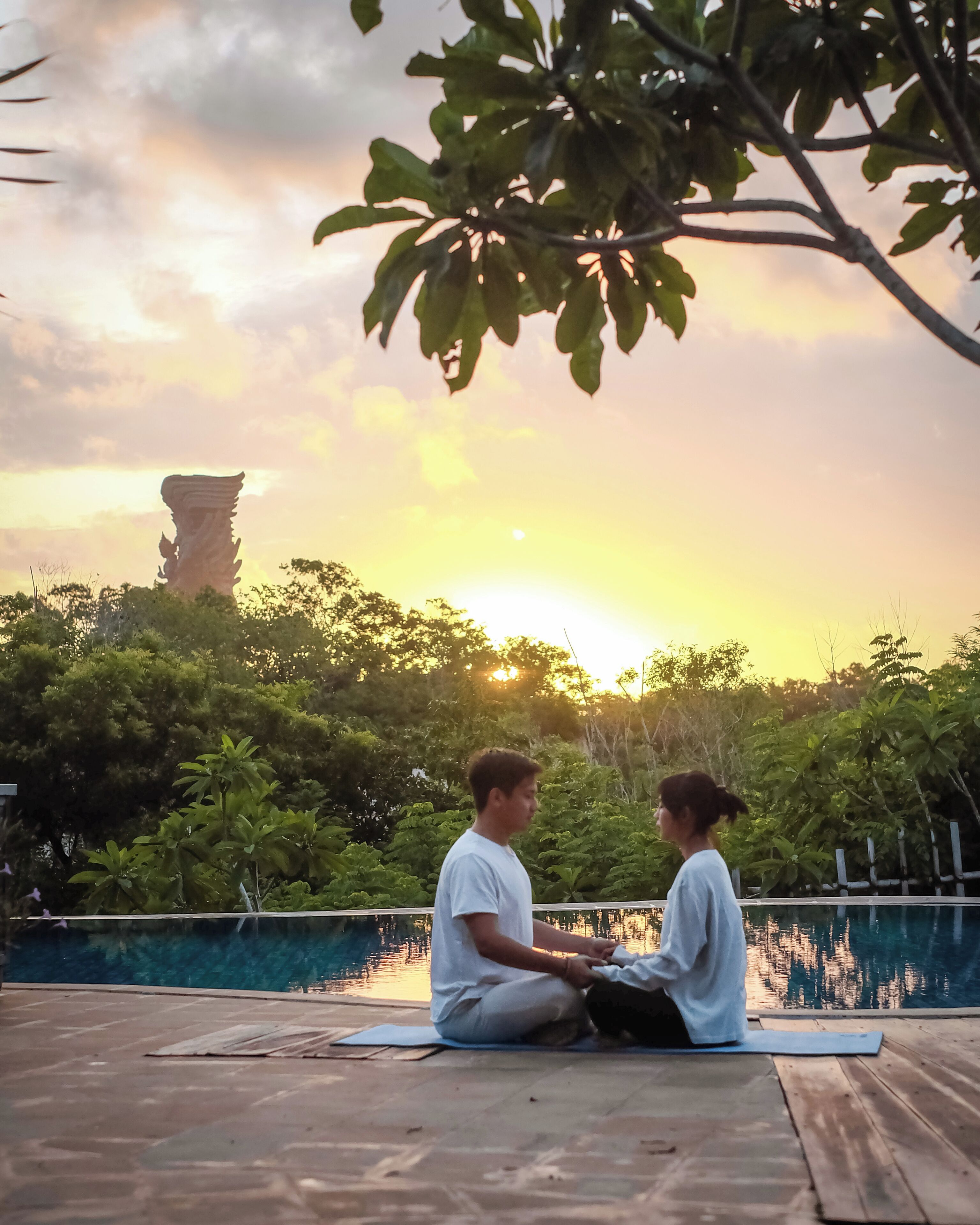 Twee personen zitten op yogamatten, met een zonsondergang op de achtergrond.