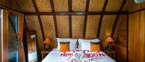 Una habitación con una cama, paredes de madera, techo tejido y una ventana.
