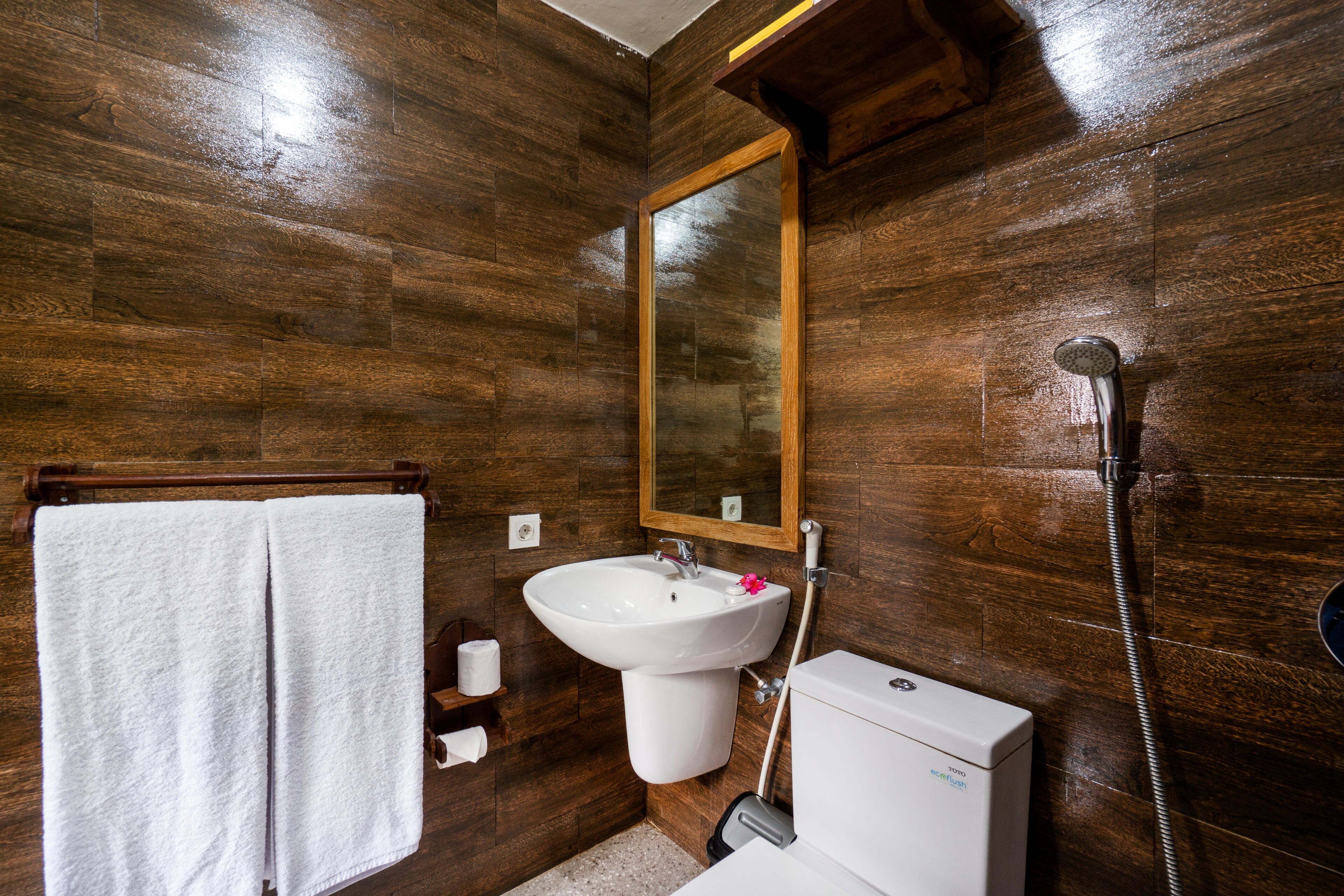 Un baño con paredes de madera, un lavamanos blanco, un espejo, un perchero para toallas y una ducha.