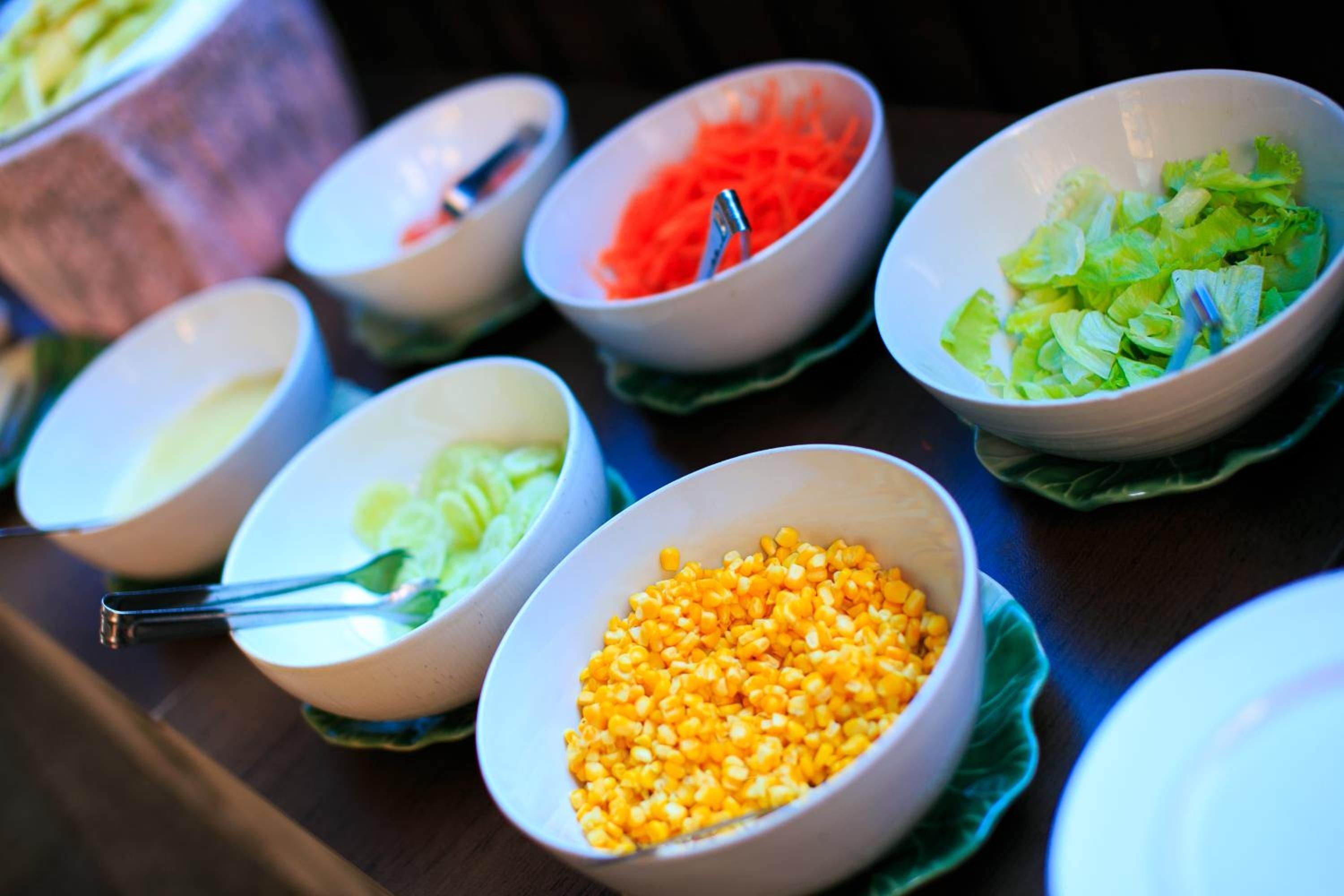 Ein Buffet mit verschiedenen Speisen in Schüsseln, darunter Mais, Karotten und Salat.