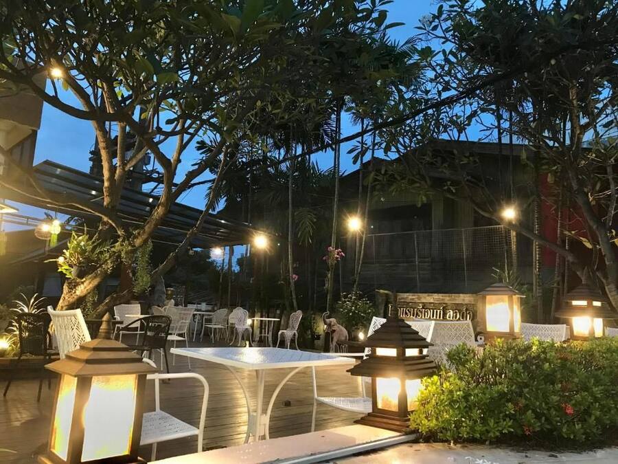 An outdoor dining area with tables and chairs, surrounded by trees and illuminated by lanterns.