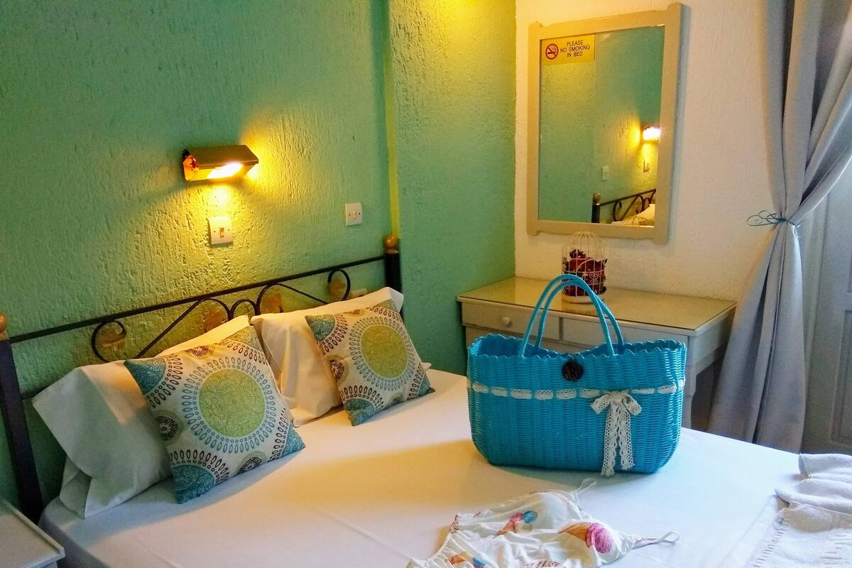 A hotel room with a bed, pillows, a nightstand, a blue basket, a mirror, and a sign prohibiting smoking in bed.
