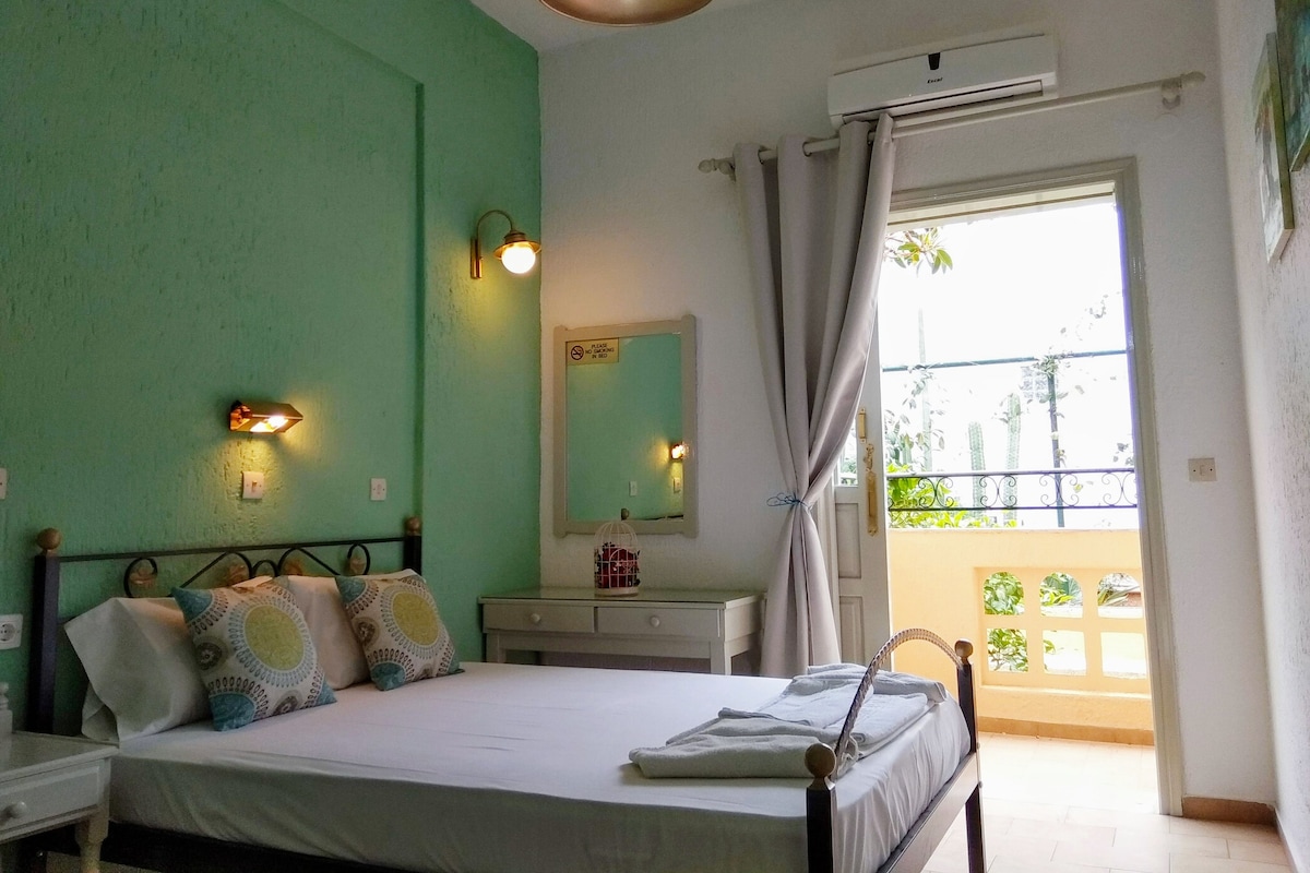 A bedroom with a bed, bedside table, lamp, and a view of a balcony.