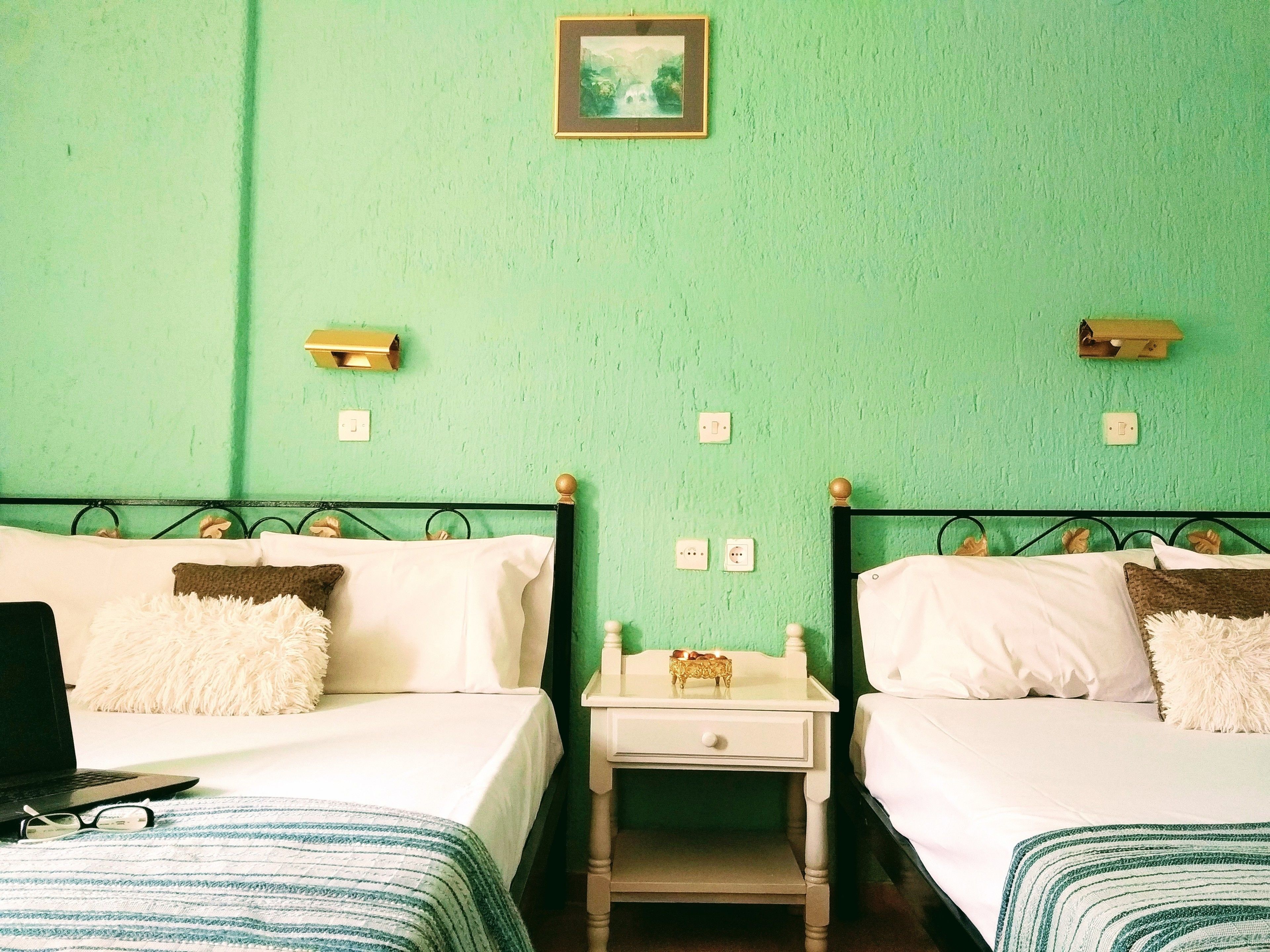 A room with two beds, each with a white and brown pillow, a small bedside table with a lamp, and a framed picture on the wall.
