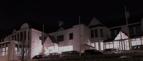 A row of white buildings with large windows and a stone wall in the foreground.
