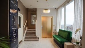 A hotel lobby with a staircase, a reception desk, a green sofa, and a view of the city through large windows. - The Mount Rooms (Barry)
