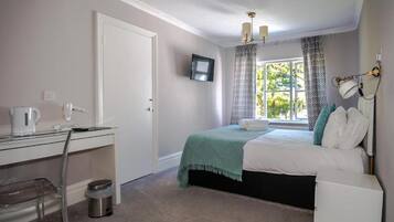 Une chambre à coucher comprenant un lit, un bureau, une chaise, un téléviseur fixé au mur et une fenêtre avec des rideaux.