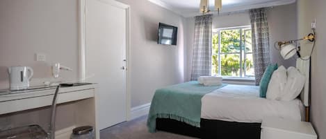 A bedroom with a bed, a desk, a chair, a TV mounted on the wall, and a window with curtains.