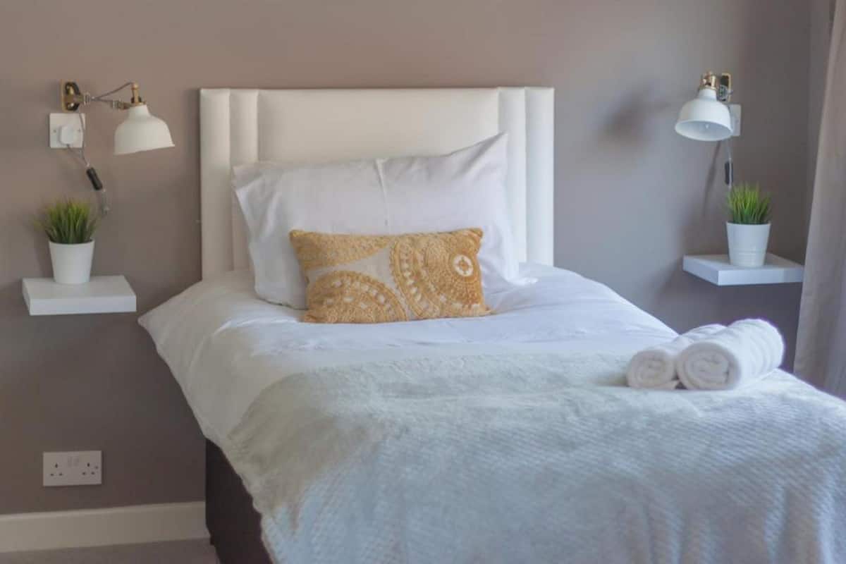 A neatly made bed with white bedding and a patterned pillow, flanked by two bedside tables with lamps and potted plants.