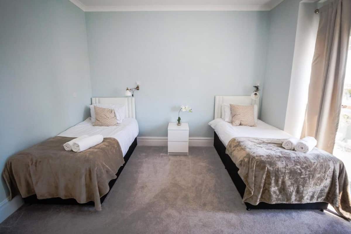 A twin bedroom with two beds, a small bedside table with a vase, and a window with curtains.