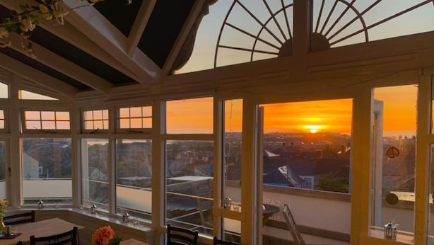 A sunlit room with large windows, a wooden table, and chairs. - The Mount Rooms (Barry)