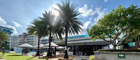 A resort with outdoor seating, palm trees, and a building with a blue roof.