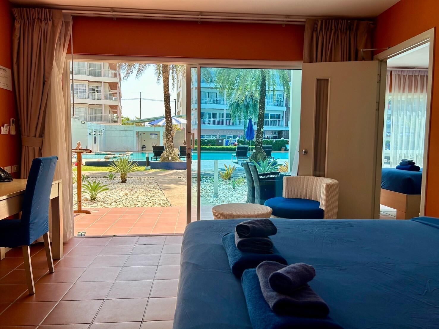 Habitación de hotel con cama, escritorio y vistas a una piscina y palmeras.