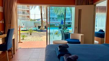 Habitación de hotel con cama, escritorio y vistas a una piscina y palmeras.